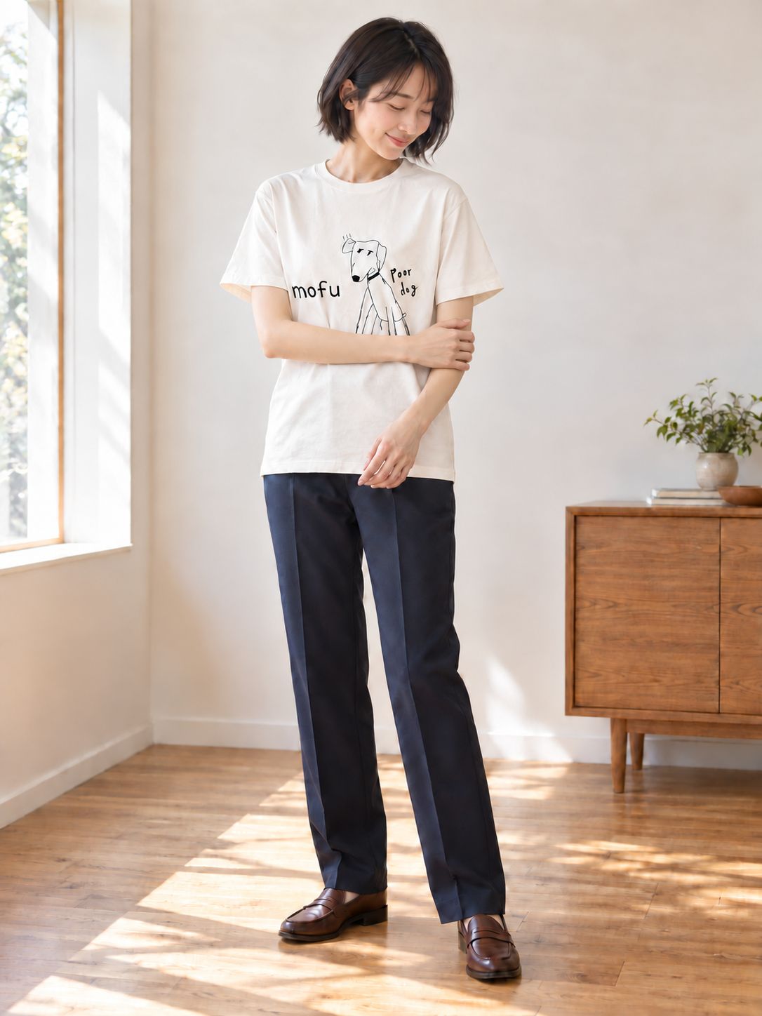 バニラホワイトのPoor dog Tシャツを着て、腕を軽く組んで立つ女性の全身